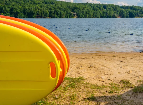 Montón de paddleboards amarillos y naranjas en la playa de arena junto a un lago — Foto de Stock