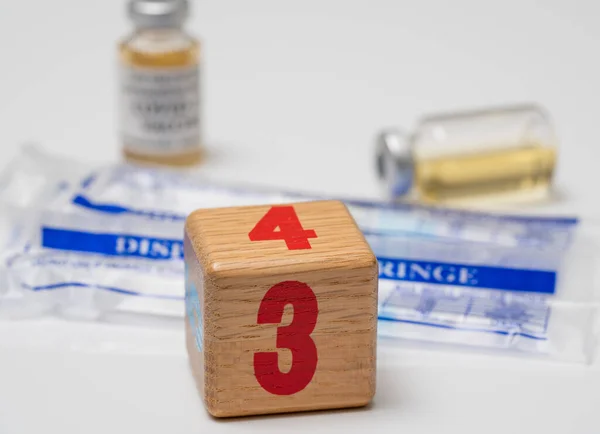 Concept for Covid-19 booster dose or shot using wooden three block with wrapped disposable syringes — Stock Photo, Image