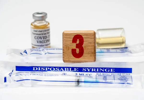 Concept for Covid-19 booster dose or shot using wooden three block with wrapped disposable syringes — Stock Photo, Image