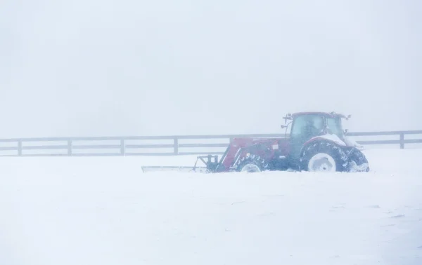 Moderní traktor s pluhem zúčtování silnici v blizzard — Stock fotografie