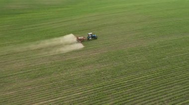 Gün batımında soya tarlası otlarını ilaçlayan bir tarım traktörünün hava görüntüleri. Ukrayna, Avrupa 'nın tarım bölgesi. Sinematik drone çekimi. UHD 4k video 'da çekildi. Güzel toprak.