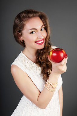 Portrait of girl in white dress with red apple. Beautiful brunette girl in studio. clipart