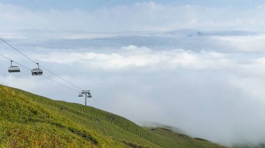 Stoos, İsviçre 'de bulutlar ve yemyeşil tepelerle çevrili bir teleferiğin manzarası..