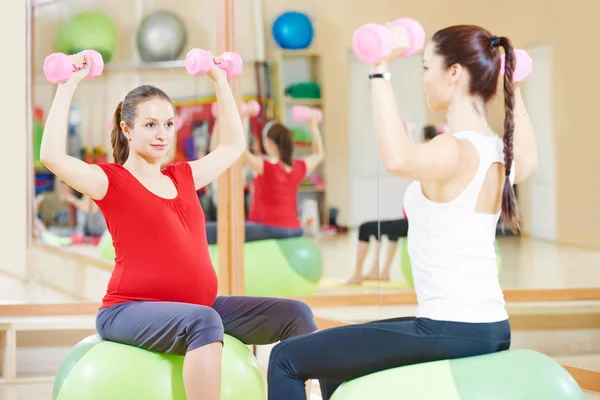 Mujer embarazada con instructor haciendo ejercicio de pelota de fitness —  Fotos de Stock