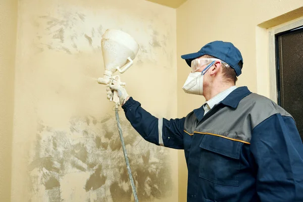 Painter spraying paint on wall indoors — Stock Photo, Image