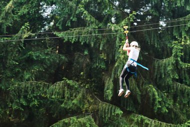 Girl riding cableway in forest adventure high wire park clipart