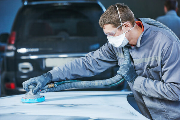 авторемонтник шлифует капот автокузова
