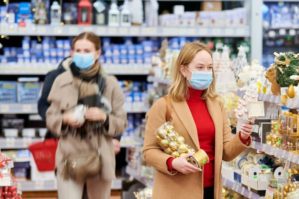 Kobieta w masce kupuje nowy rok dekoracji w sklepie na zamknięcie koronawirusa. — Zdjęcie stockowe