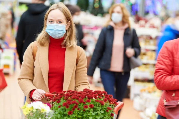 Mulher na máscara que compra flores para jardinagem doméstica na loja no fechamento do coronavírus. — Fotografia de Stock