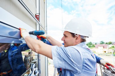 worker builder installing glass windows on facade