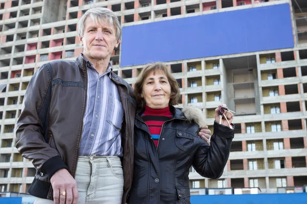 Starsza Kaukaska Para Stojąca Kluczami Ręku Przeciwko Niebieskiemu Transparentowi Budynku — Zdjęcie stockowe