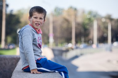 Granit kaldırımın kenarında oturan genç bir çocuk.
