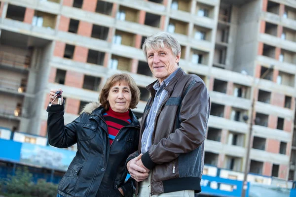 Anahtarlarını Gösteren Yaşlı Çift Inşaat Halindeki Binaya Karşı Ayakta Duruyor — Stok fotoğraf