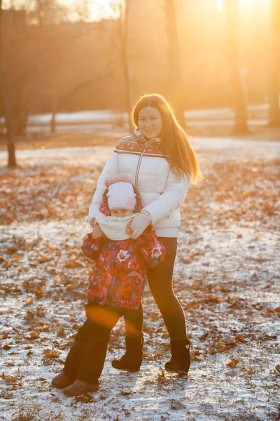 夕日の下で冬の公園に立つ6歳の娘の母親 — ストック写真