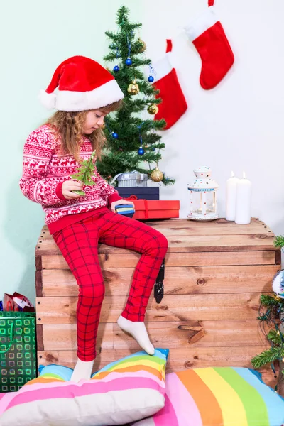 圣诞节的时候 一个戴着红色圣诞帽的漂亮姑娘在自家房间的木箱上玩耍 — 图库照片