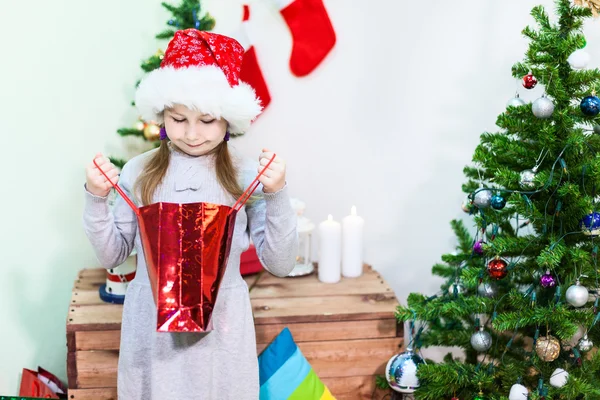 Cute Uśmiechnięta Dziewczyna Czerwonym Kapeluszu Mikołaja Patrząc Wewnątrz Worka Prezentów — Zdjęcie stockowe