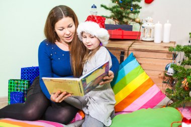 Kafkasyalı anne, Noel 'den önceki gece yeşil ağacın yanında kitap okuyor.