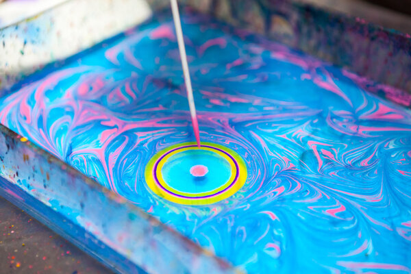 Close up view of making circle on water surface with stick and color inks