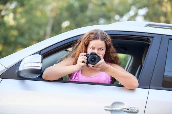 カメラを手にしたピンクのTシャツを着た喜びの女性が車から写真を撮る — ストック写真