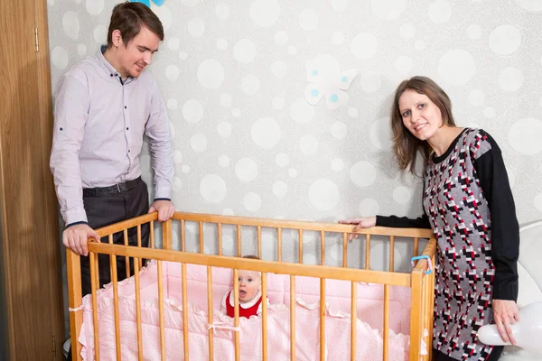 Baby Girl Sentada Cama Con Dos Padres Pie Alrededor —  Fotos de Stock