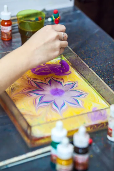 Painter working with basin for water surface marbling, drawing flower