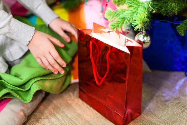 小朋友的手伸向树下的红色圣诞礼品袋 — 图库照片