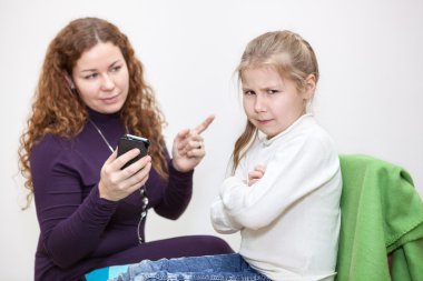 Kızgın kız, annesinin yanına cep telefonunu alarak oturuyor.