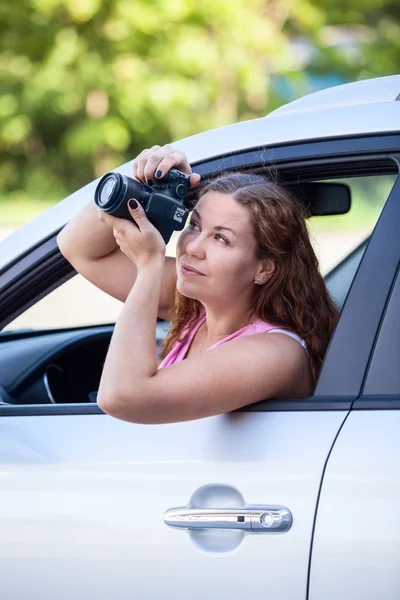 年轻的女人坐在车里 用数码相机从窗户上拍照 — 图库照片