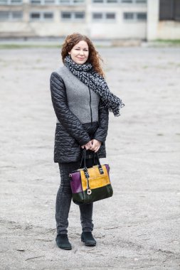 Beyaz kıvırcık saçlı kadın elinde torbayla kameraya bakıyor.