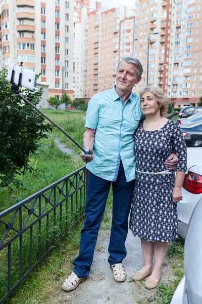 Dos personas maduras que utilizan palo para selfie fotografías mediante la colocación de un teléfono inteligente —  Fotos de Stock