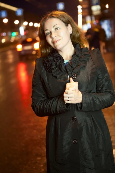 Hübsche Frau, die das Auto erwischt, während sie auf dem Bürgersteig in der nächtlichen Stadt steht und weit weg schaut — Stockfoto