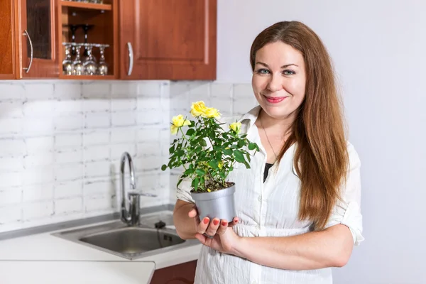 Γυναίκα νοικοκυρά στέκεται στην κουζίνα, κρατώντας τα κίτρινα τριαντάφυλλα στο ποτ στα χέρια — Φωτογραφία Αρχείου