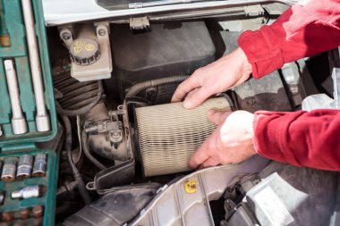 Tamirci elleri araba motorunun hava kutusundan kirli hava filtresi kâğıt kartuşlarını çıkarıyor.