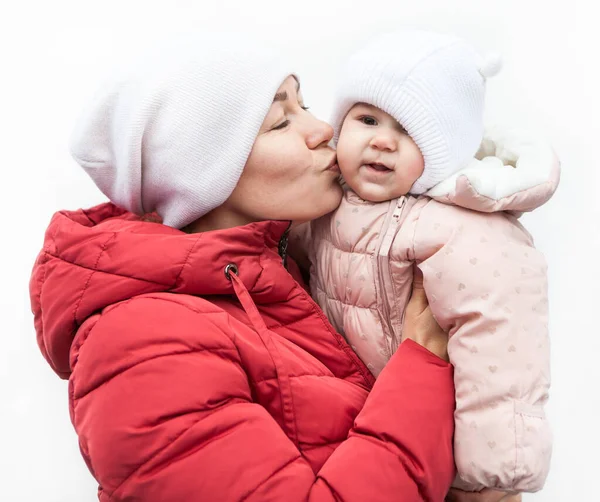 妈妈和女儿穿着寒冷天气的衣服站在白色的背景上 妈妈抱着孩子亲吻她的孩子 — 图库照片