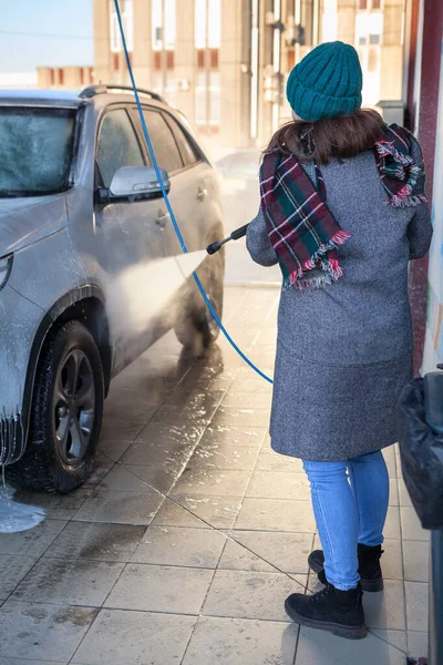 在寒冷季节 一个迷人的白种人女人用高压软管在自助加油站洗车 — 图库照片