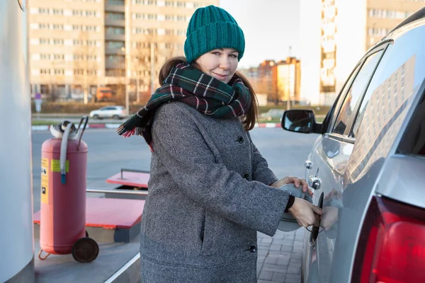 Caucasian woman opening cap lid of car tank on petrol station, winter season, female looking at camera, winter season