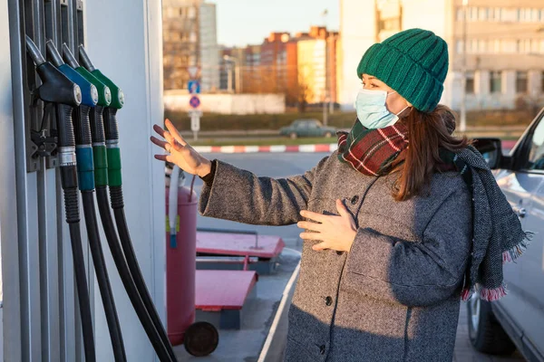 一个戴防护面罩的女人在加油站为一辆汽车选择牌子的燃料 保暖衣服 — 图库照片