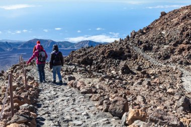 Bir grup turist Teide volkanının zirvesinden lav yığınının arasındaki taş bir merdiven boyunca iniyor. Rüzgâr geçirmez kıyafet yürüyüşü yapan üç kişi. Tenerife Adası, Kanarya Adaları, İspanya