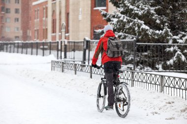Karlı şehir caddesinde bisiklet süren yetişkin bir adamın kışın sırt çantalı bisikletli görüntüsü.
