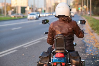 Genç bir kadın motosiklet sürmeye hazırlanıyor, bisiklete biniyor, dikiz aynasından bakıyor.