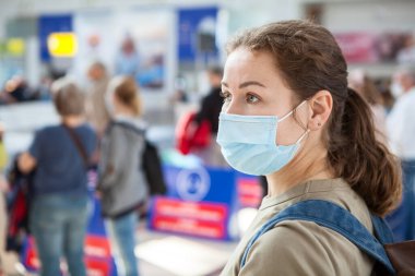 Beyaz kadın portresi, güvenlik maskesi takan kadın uluslararası bir havaalanı salonunda duruyor.