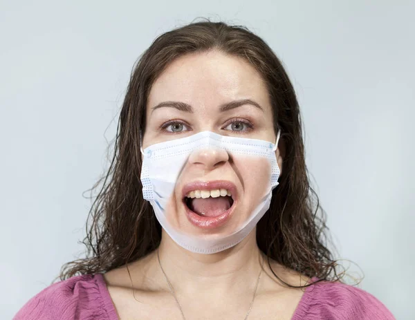 Irritation and disgust are on the face of an adult woman under medical mask with calm eyes. Supposition of real emotion while wearing mask. Portrait on a grey background, emotions series