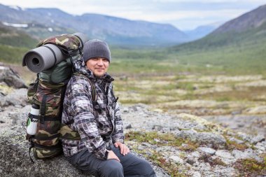 Dağ vadisinde kayaların üzerinde eğlenen sırt çantalı yorgun bir adamın portresi.