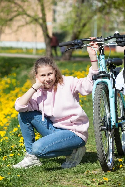 Веселая Красивая Девушка Розовой Толстовке Сидит Дорожке Голубым Велосипедом Смотрит — стоковое фото