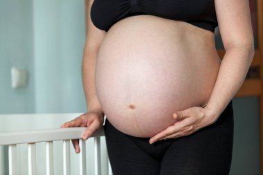 Genç hamile bir kadın bebek yatağının yanında duruyor. Çocuk odası arka tarafta.