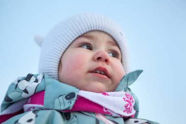 Sıcak şapka ve eşarp takan küçük bir çocuğun düşük açılı portresi. Kış mevsiminde yanaklarıyla donmuş burnu okumak. Beyaz kız.