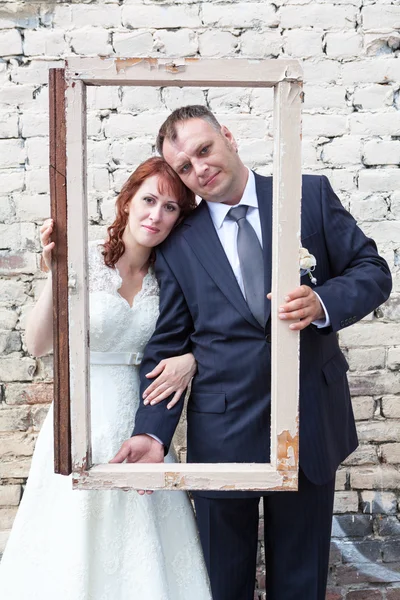 Casal recém-casado olhando através do frame de retrato — Fotografia de Stock