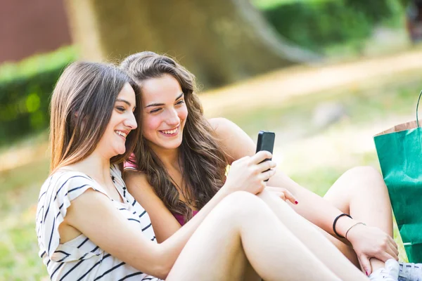 Две девушки смотрят на смартфон в парке — стоковое фото