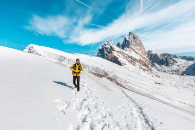 Karlı dağın tepesinde yürüyüş yapan adam - Sarı bir ceket giyen mutlu yürüyüşçü arka planda güzel bir manzarayla karda yürüyor - uzak bölgelerde macera ve seyahat kavramları