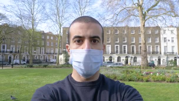 顔のマスクを持つ若い男の肖像 ロンドンの公園で医療マスクを身に着けている男 コロナウイルスパンデミックの間のライフスタイルと医療 — ストック動画
